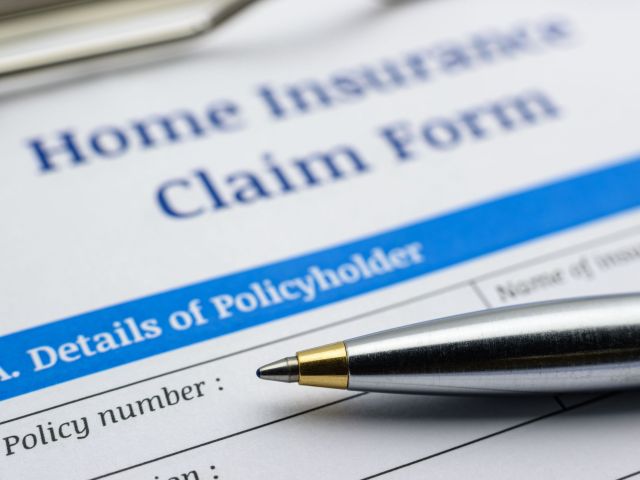 Blue ballpoint pen and a home insurance claim form on a clip board. A blank / empty form is waiting to be filled and signed by a policyholder / insured person.
